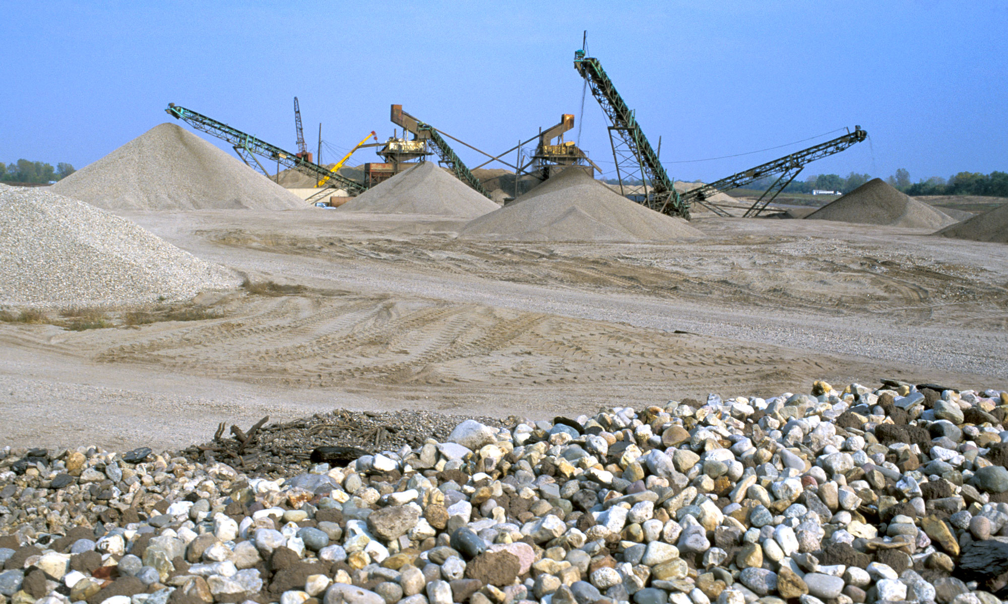 Quarry with gravel in foreground, cranes in background.