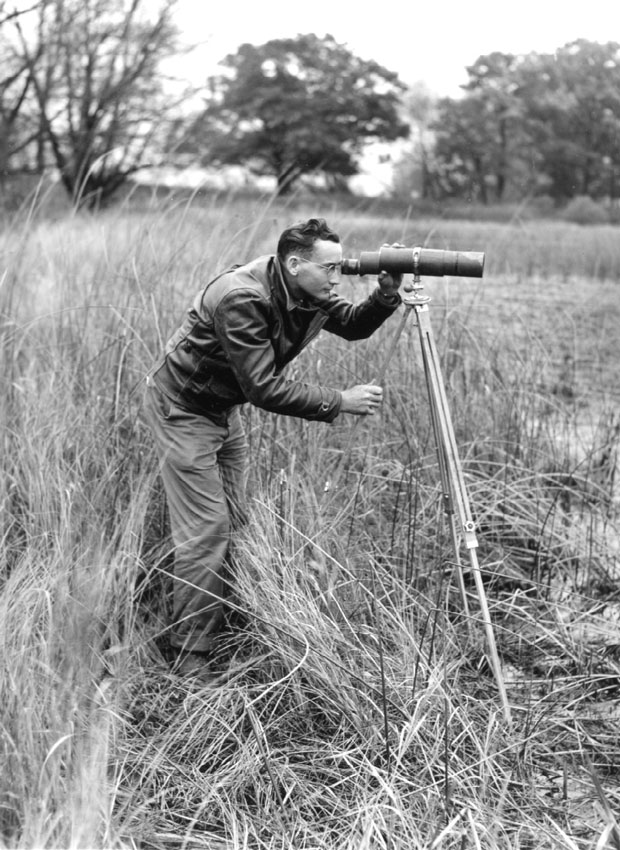 Man looking through scope on shore, 1942.