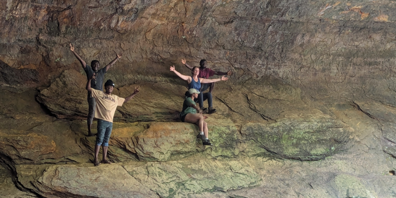 Students inside a cave, their arms outstretched.